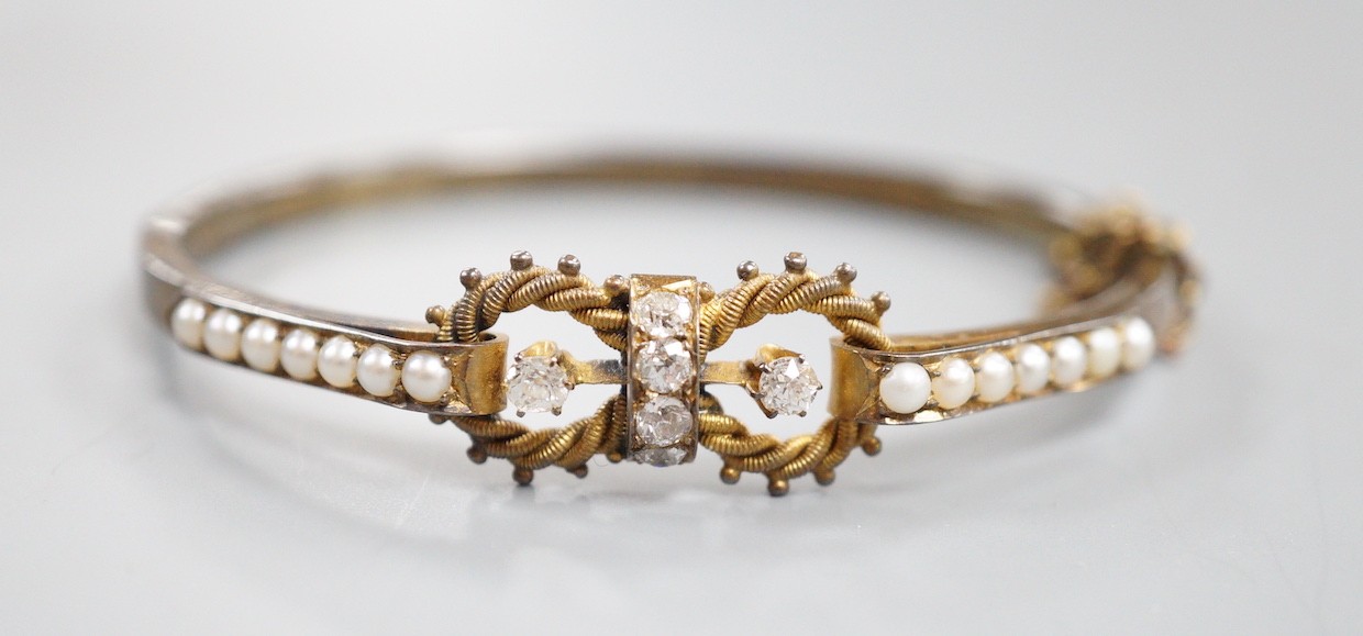 A late Victorian yellow metal, six stone diamond cluster set hinged bangle, with split pearl set shoulders, interior diameter 56mm, gross weight 10.5 grams.